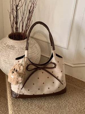 Tan polka dot shoulder bag with brown trim, bow detail, and fuzzy charm.