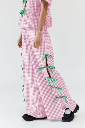 Blush pink gingham wide-leg trousers with green bow details down the side seams.