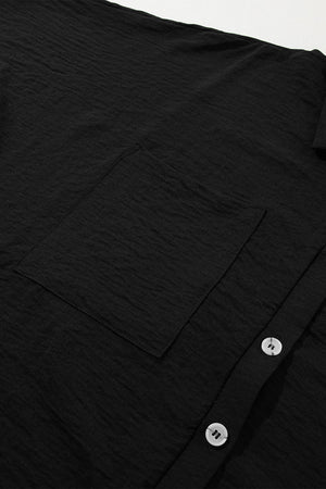 Black oversized shirt romper with textured fabric, button front, and chest pocket.