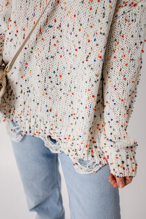 Confetti knit sweater in white with colorful flecks and distressed hem detail.