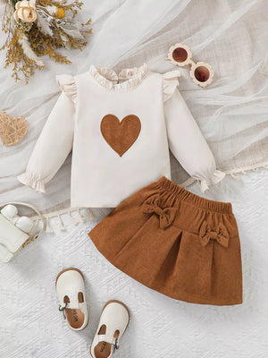 Baby girl's cream ruffle top with brown heart applique and brown corduroy skirt with bows.