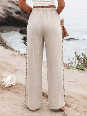 Relaxed beige linen wide-leg trousers with drawstring waist and beaded side detail.
