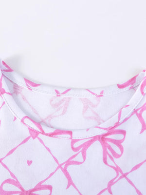 Baby dress with pink bow and heart print on white cotton fabric.