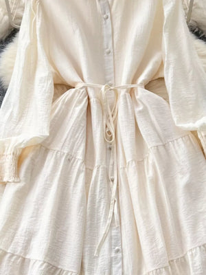 Off-white tiered long sleeve button-down dress with tie waist and textured fabric.