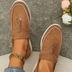 Brown flat slip-ons with decorative strap and tassel detail.