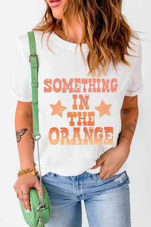 White graphic tee with faded orange text and stars reading "SOMETHING IN THE ORANGE