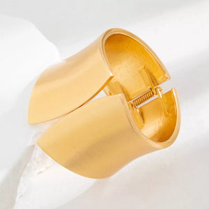 Gold-toned sculptural cuff bracelet with a wide, open design and spring hinge closure.