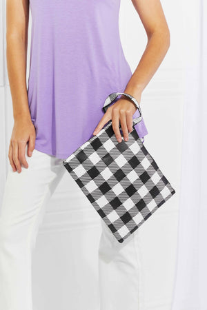 Gingham wristlet pouch with metal ring in black and white, held by a model wearing a lavender top and white pants.