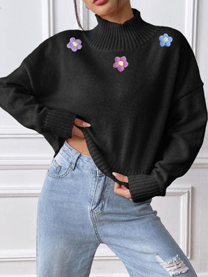Black cropped turtleneck knit sweater with embroidered floral appliques and ribbed cuffs.