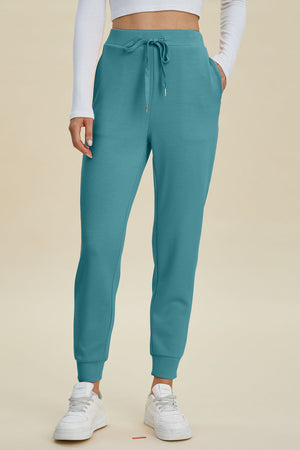 Teal joggers with drawstring waist and cuffed ankles, styled with white sneakers.