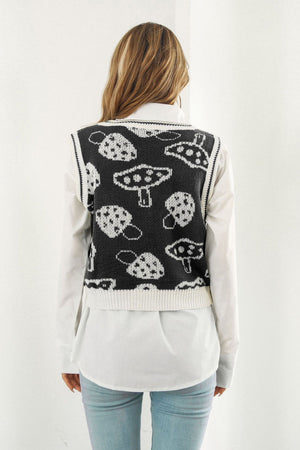 Black knit vest with white mushroom motif, ribbed trim, worn over a white shirt.
