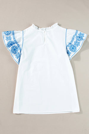 White blouse with embroidered blue floral sleeves and ruffle neckline
