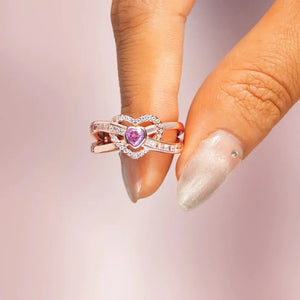 Rose gold ring with intertwined hearts, pink center stone, and clear cubic zirconia accents.