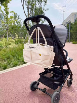 Beige canvas shopper bag with multiple pockets and a smiley face detail, hanging from a stroller.