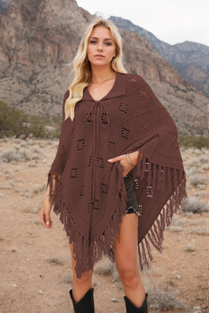 Brown knit poncho with geometric pattern, fringe, and tie neck, styled with shorts and boots.
