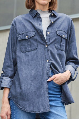 Relaxed denim shirt in navy with patch pockets and buttoned cuffs, worn over a grey top.