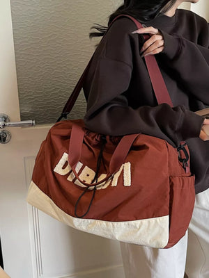 Chic color-blocked travel bag in rust with cream bottom and white textured lettering.