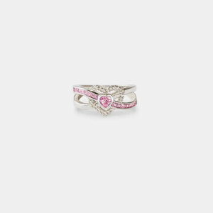 Silver ring with intertwined infinity band and a pink heart-shaped zirconia center surrounded by small clear stones.
