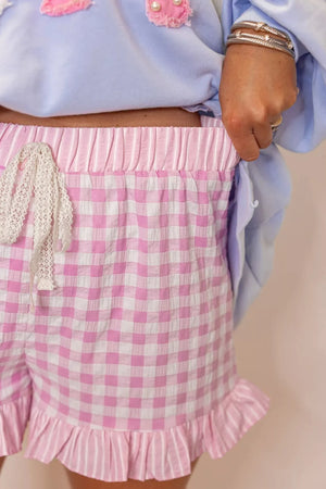 Charming gingham chino shorts in blush pink with ruffle hem and drawstring detail.