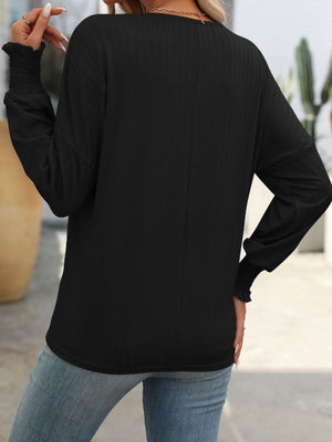 Black textured blouson top with smocked cuffs and long sleeves.