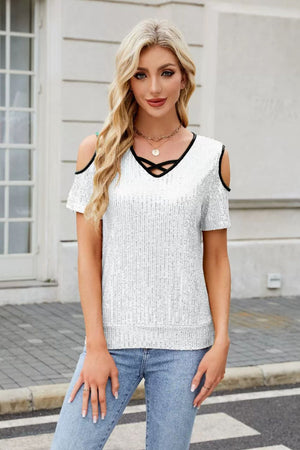 White sequin cold shoulder blouse with black trim and criss-cross neckline.