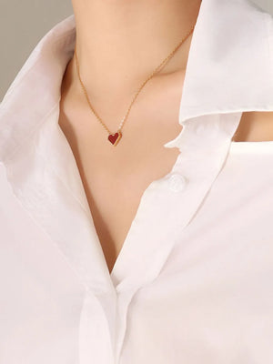 Gold necklace with a small crimson heart pendant on a white collared shirt.