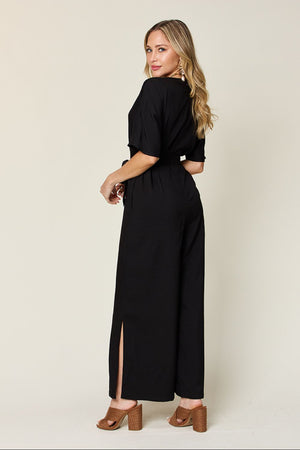 Black wrap jumpsuit with short sleeves, belted waist, and slit wide legs.