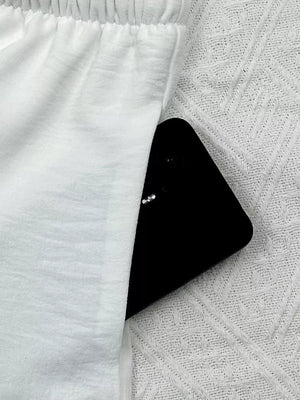 White relaxed fit maternity pants with elastic waistband and side pocket holding a phone.