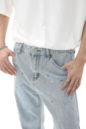 Light wash denim trousers with colorful paint splatters and a slouchy fit.