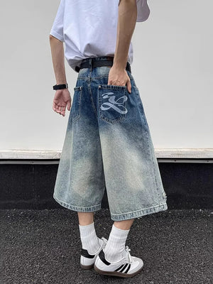 Men's distressed wide-leg denim shorts with gradient wash and graphic back pocket detail.