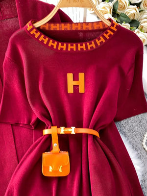 Burgundy knitted maxi dress with orange trim and belt featuring a mini bag accessory.