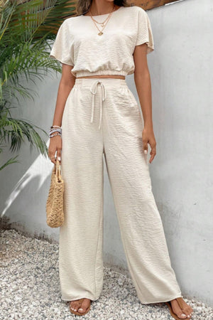 Beige textured crop top and wide-leg trousers with drawstring waist, styled with layered necklaces.