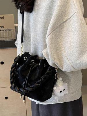 Black bucket bag with chunky chain trim and fluffy charm, worn crossbody.