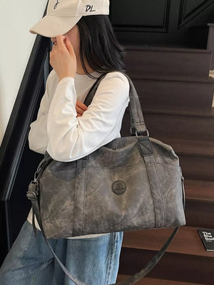 Distressed dark gray leather travel duffel bag with adjustable strap and logo detail.