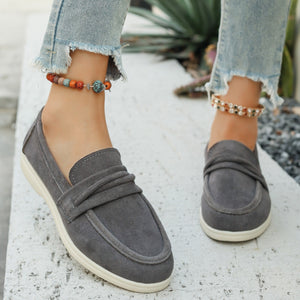 Grey slip-on loafers with ruched strap detail and white soles.