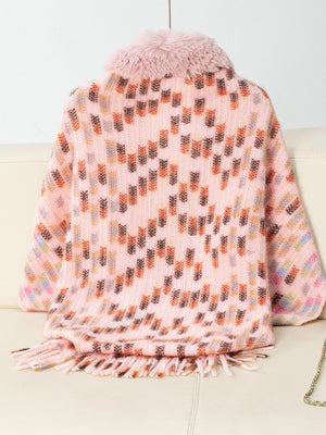 Pink acrylic knit poncho with faux fur collar and fringe hem, featuring a geometric pattern.