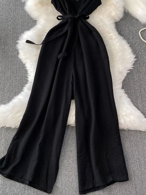 Black V-neck wide leg jumpsuit with belted waist and button details.