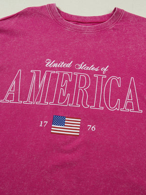 Patriotic graphic cotton t-shirt in pink with "United States of America" text and US flag graphic.