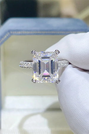 Emerald cut moissanite ring in silver with pave band and four-prong setting.