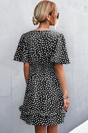 Black smocked waist mini dress with white speckle print and flutter sleeves.