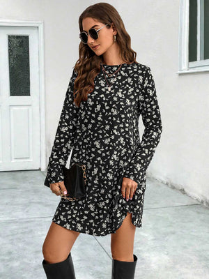 Black floral swing mini dress with long sleeves and side slit, styled with a clutch.