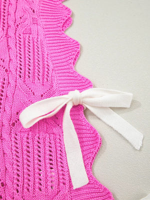 Chic pink openwork knit sweater vest with cable knit detail and white tie closure.