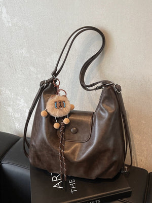 Slouchy coffee brown pu leather shoulder bag with braided detail and lion charm.