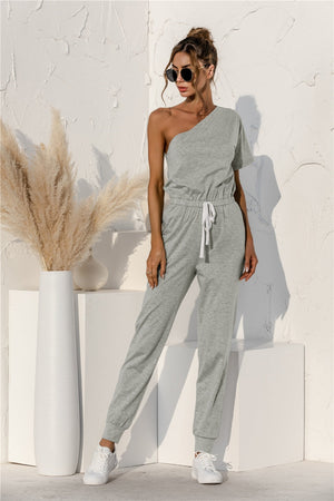 Gray asymmetric sweat jumpsuit with drawstring waist and cuffed jogger legs.
