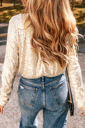 Sequin wrap bodysuit in ivory with long sleeves and deep V-neck, worn with jeans.