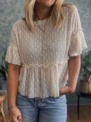 Beige textured blouse with ruffle hemline and short flutter sleeves, styled with jeans.