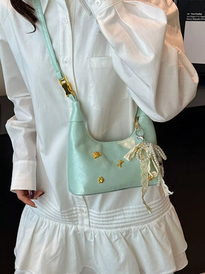 Light green mini hobo bag with gold accents and pearl charm, worn with a white dress.