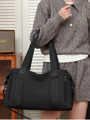 Black Oxford cloth travel bag with zippered side pockets and dual handles.