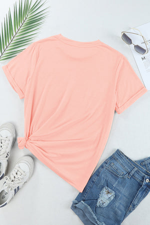 Watermelon pink graphic tee with rolled sleeves and a knotted hem, styled with denim shorts and sneakers.
