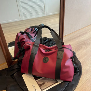 Burgundy canvas duffel bag with black straps and a circular logo patch.
